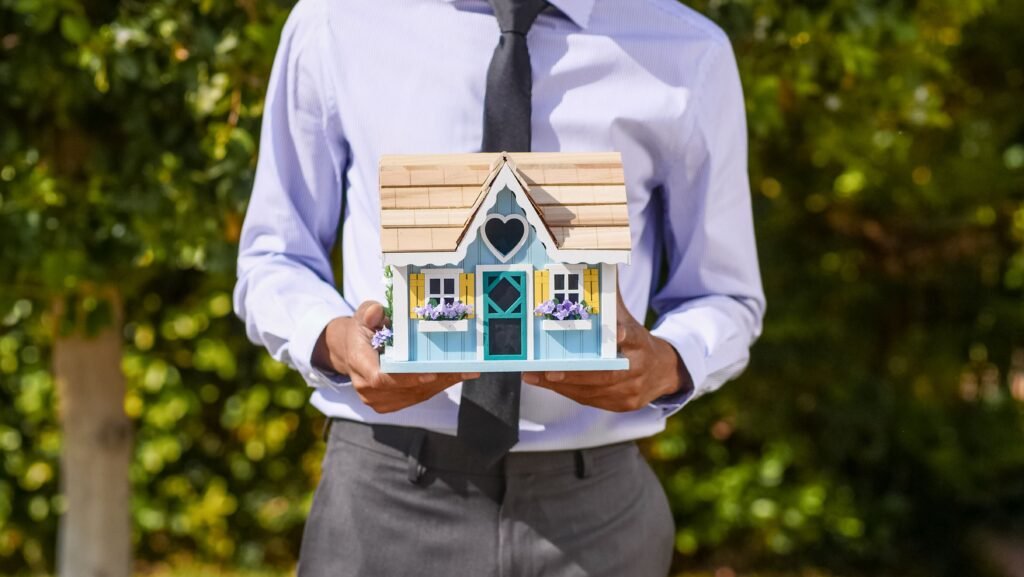 A business professional holds a decorative miniature house, symbolizing real estate investment.